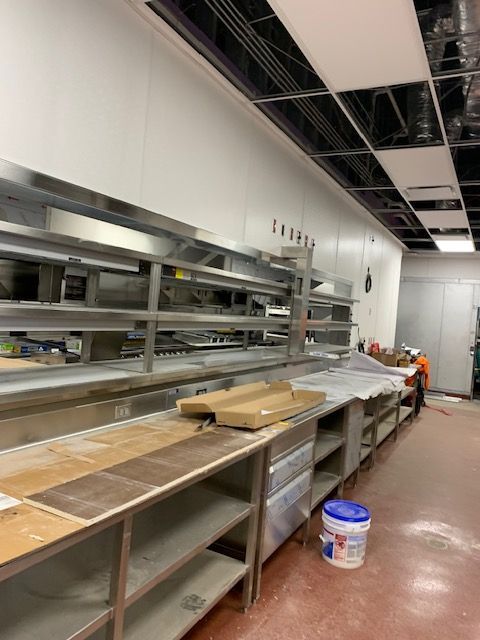 Commercial kitchen under construction, stainless steel counters and shelving.