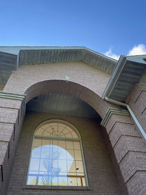 Brick building with large arched window, arched brick detail, and blue sky.