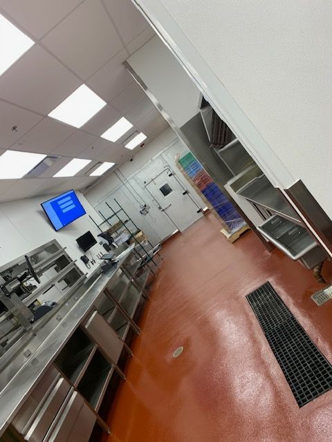 A commercial kitchen with stainless steel counters, red floor, and white walls.