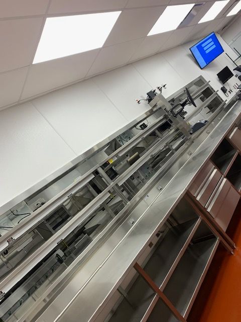 Overhead view of a long, metallic conveyor belt system, likely in a store or checkout area.