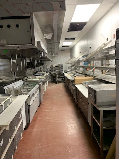 Empty commercial kitchen with stainless steel appliances, red floor, and overhead ventilation.