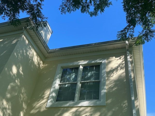 Light yellow house corner with white trim, window, and blue sky.