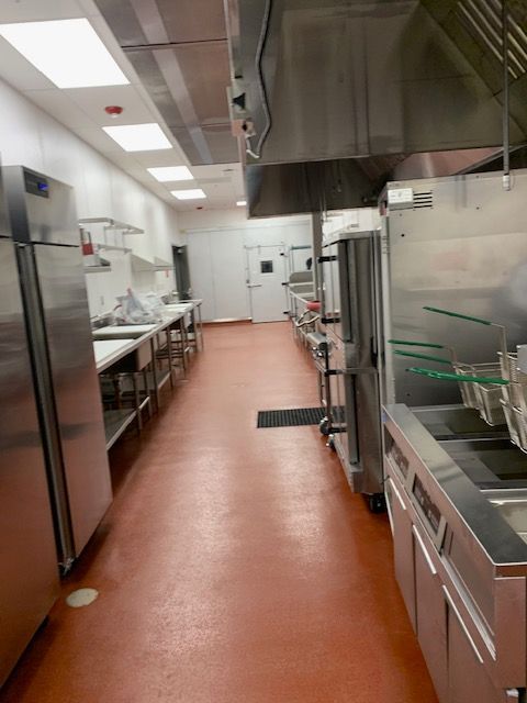 Empty commercial kitchen with stainless steel appliances, shelving, and orange flooring.