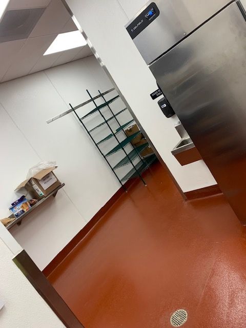 Empty commercial kitchen with orange floor, stainless steel appliances, and shelving.