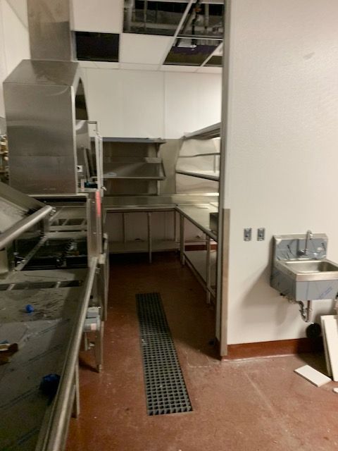 Interior view of an industrial kitchen with stainless steel equipment and shelves; red floor.