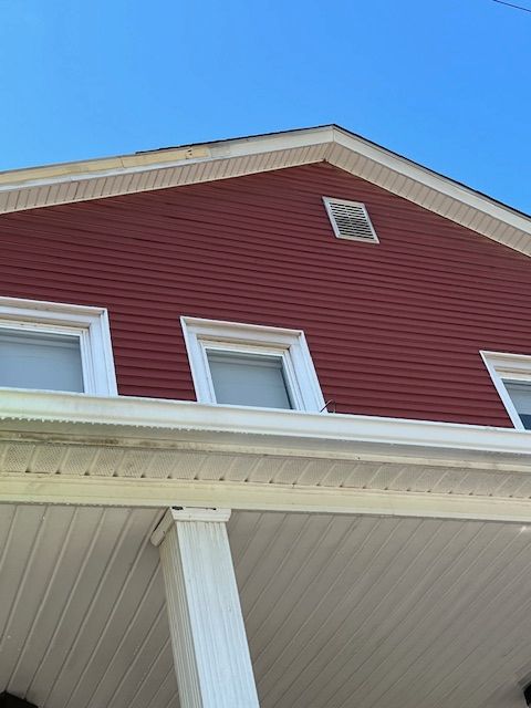 Red siding of a house with white trim, windows, and soffit under a clear, blue sky.