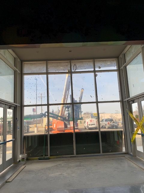 Exterior view through large windows of construction site with crane and vehicles.