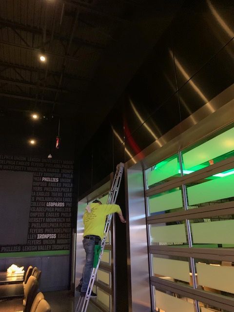 A person in a yellow shirt climbs a ladder next to a green-lit wall.