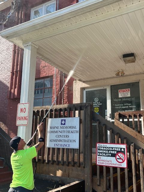 Man pressure washing a building's awning. Sign for health center administration entrance.