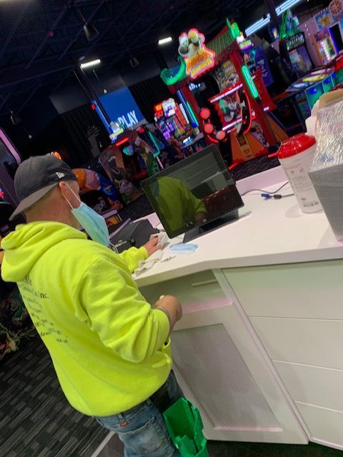 Person in neon green hoodie, mask, and hat, at arcade counter, looking at a screen.