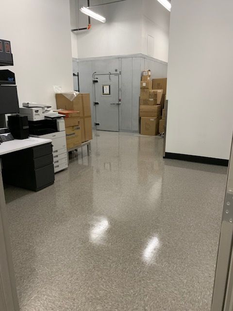 A brightly lit room with a shiny gray floor, boxes, and a walk-in cooler in the background.