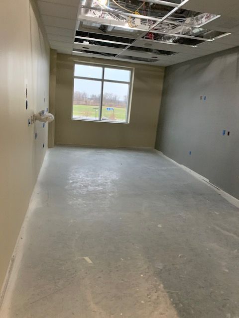 Empty room with a window, unfinished ceiling, and concrete floor. Walls are painted gray and beige.