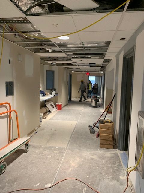 Construction site hallway with exposed ceiling and workers. Light walls, concrete floor, equipment.
