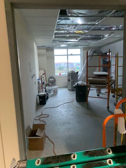 Room under construction, open doorway view. Exposed ceiling, concrete floor, construction tools present.