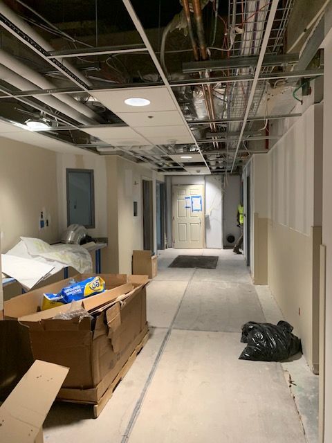 Construction of a hallway, with exposed ceiling infrastructure, unfinished walls, and materials on the floor.