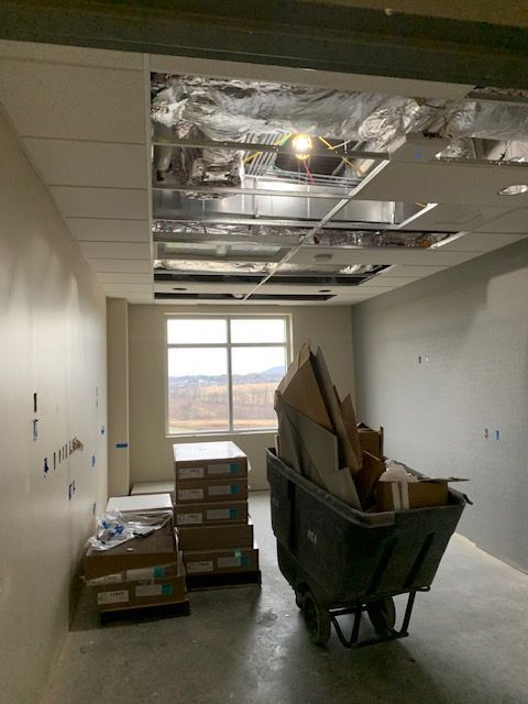 Interior room under construction with exposed ceiling, wheelbarrow full of debris, and window view.