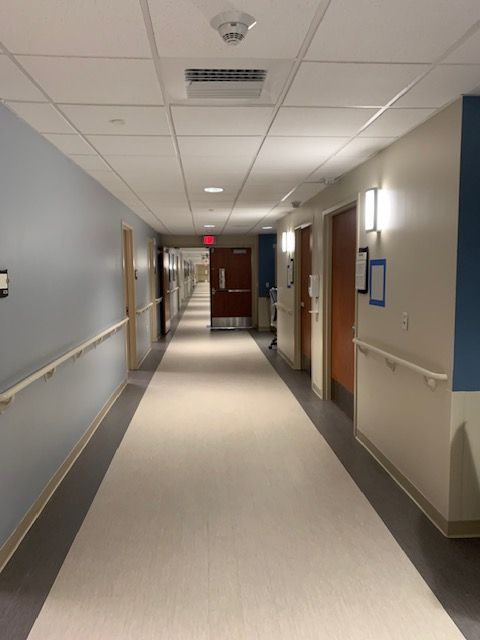 Long hospital hallway with beige floor, light blue and white walls, and wooden doors.