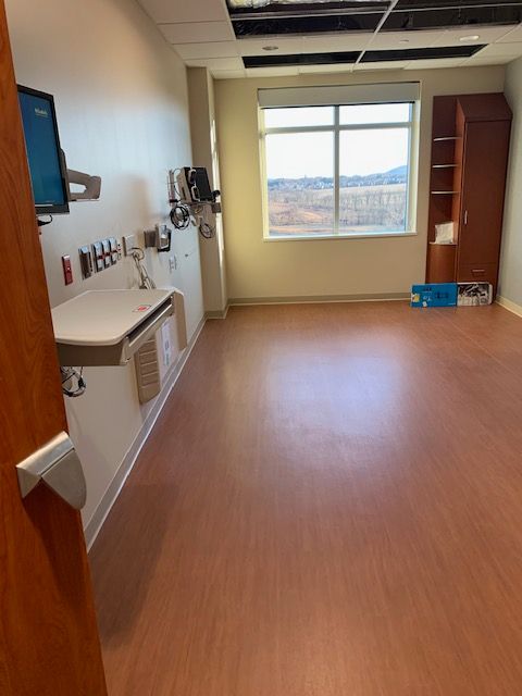 Empty hospital room with medical equipment, a window, and wood-look flooring.