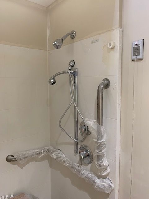Bathroom shower with grab bars and adjustable showerhead. Chrome fixtures. Beige walls.