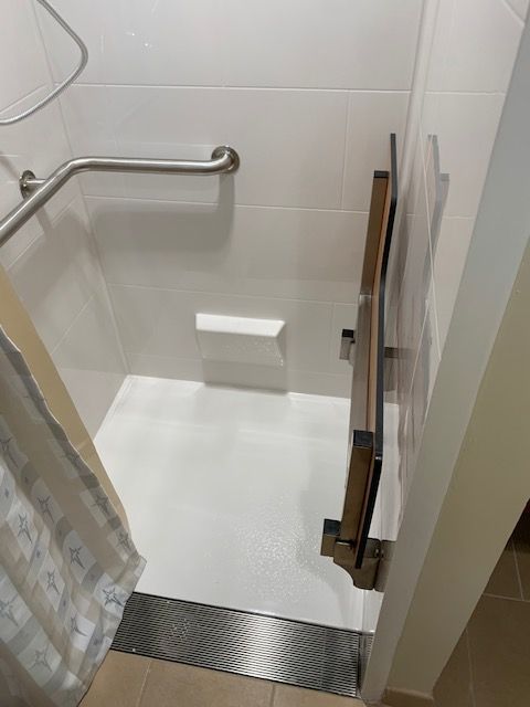 White accessible shower with a fold-down seat, grab bar, and curtain.