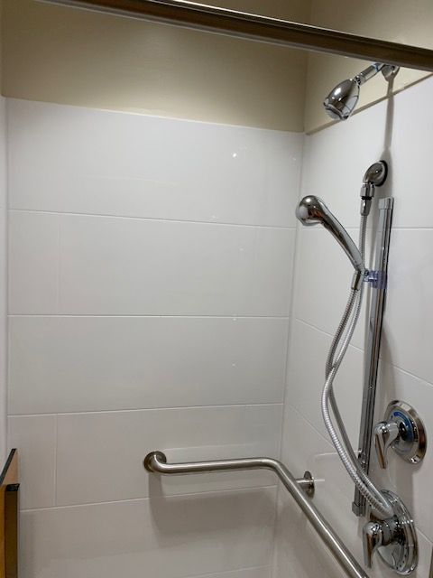Shower with white tiled walls, grab bar, adjustable shower head, and silver fixtures.