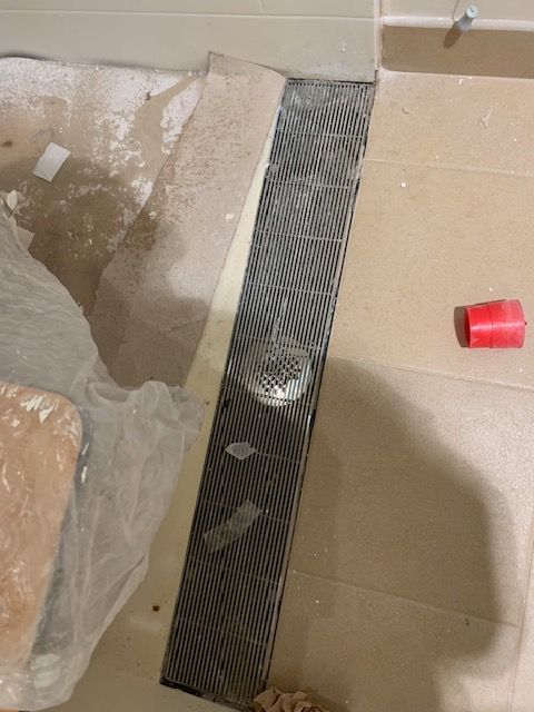 Metal grate and drain installed in a tiled floor. Construction debris and a red cap are nearby.