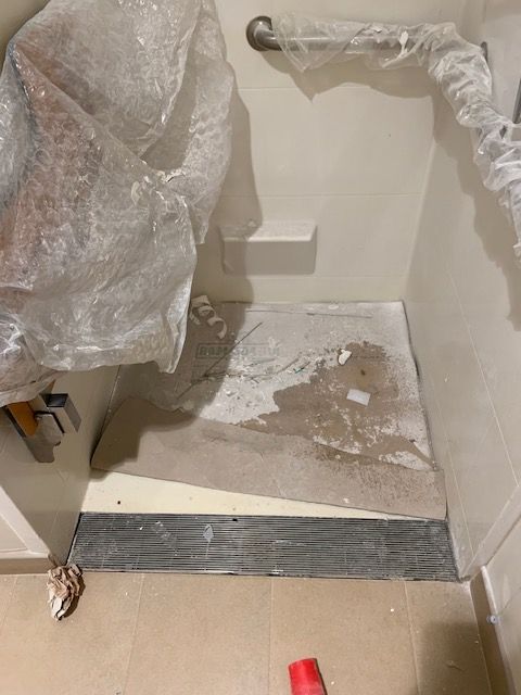 Bathroom floor under construction, with exposed concrete, plastic sheeting, and a black threshold.