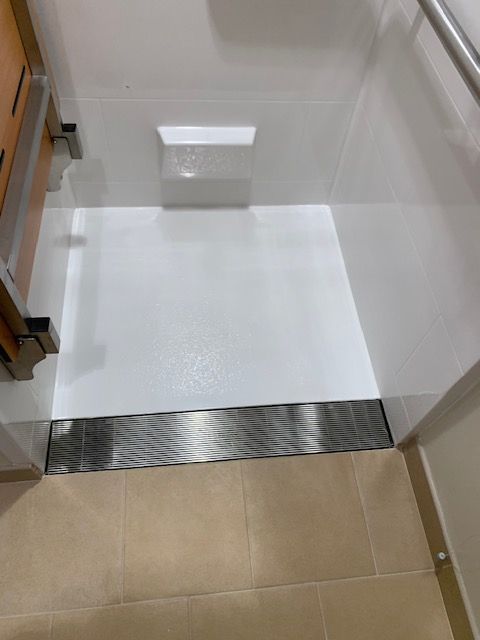 White shower with a stainless steel drain at the edge. The floor is beige tile.