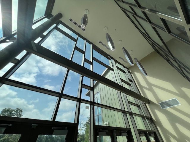 Looking up through a large glass window wall with black frames, seeing a blue sky with some clouds.