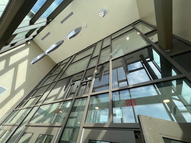 Glass-walled building entrance with geometric windows, neutral tones. Sunlight streams in.