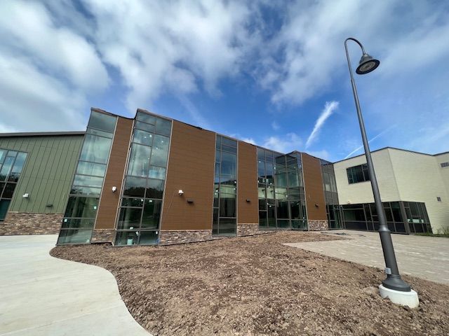 Modern building with glass and brown exterior under a blue sky. A lamp post is in the foreground.