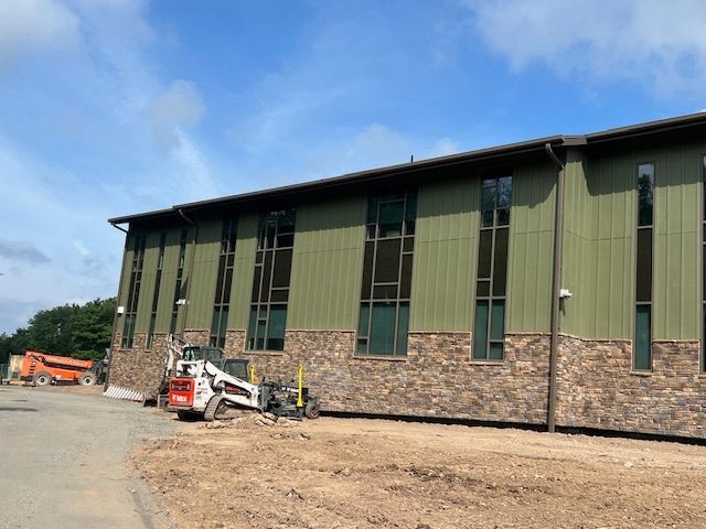 Building exterior with green siding and stone base, construction equipment in front.