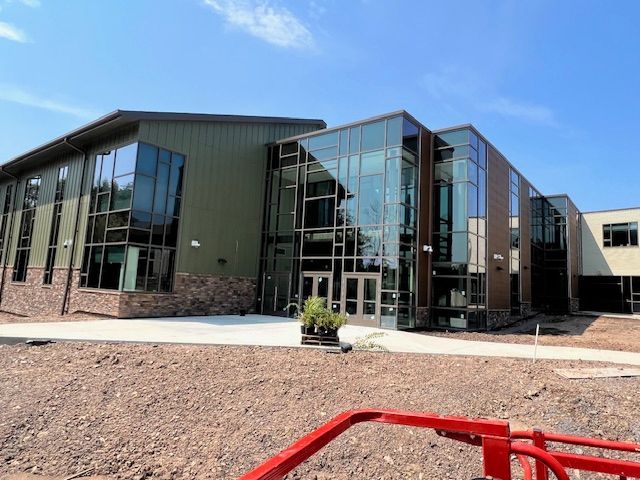 Modern school building exterior with glass walls, brick and green siding under a blue sky.