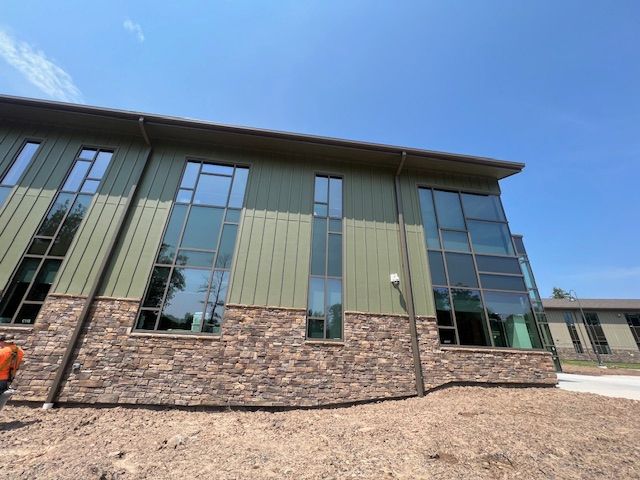 Modern building with green siding, stone base, and large windows against a blue sky.
