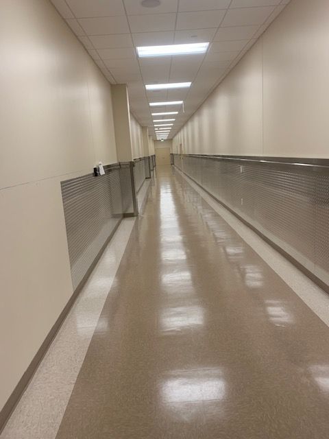 Long, empty hallway with beige walls, glossy floor, and rectangular ceiling lights.