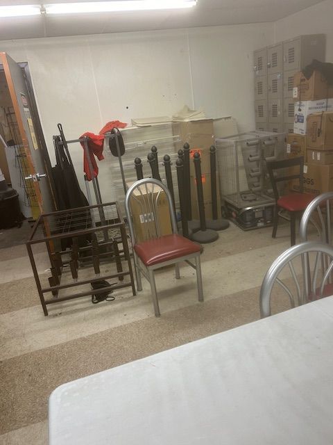 A cluttered storage room with tables, chairs, and various objects.