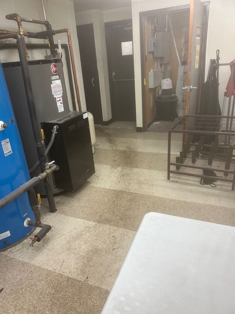 Basement with water heater, pipes, and wet floor near doors.