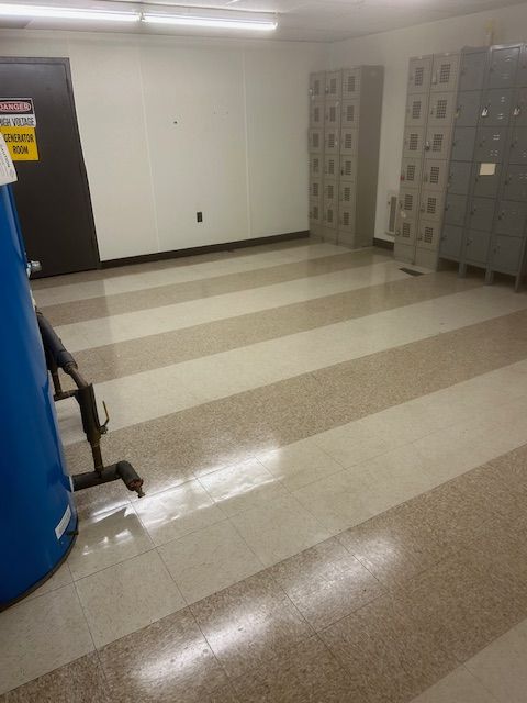 Empty room with lockers, tiled floor, blue tank, and a door with a warning sign.
