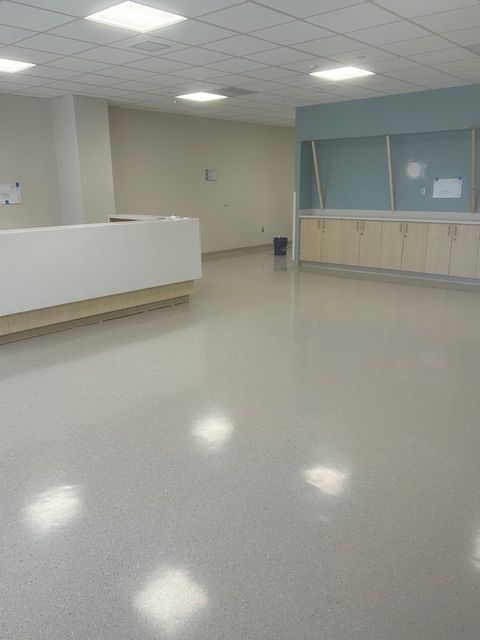 Empty, light-filled medical office space. Features a white reception desk, pale gray floor, and storage cabinets.