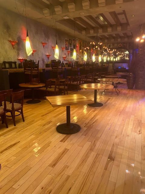 Empty restaurant interior with wooden floors, tables, chairs, and hanging lights.