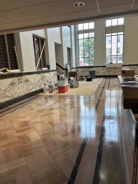 Refurbished interior with polished wood floor, marble walls, and large windows. Construction supplies visible.