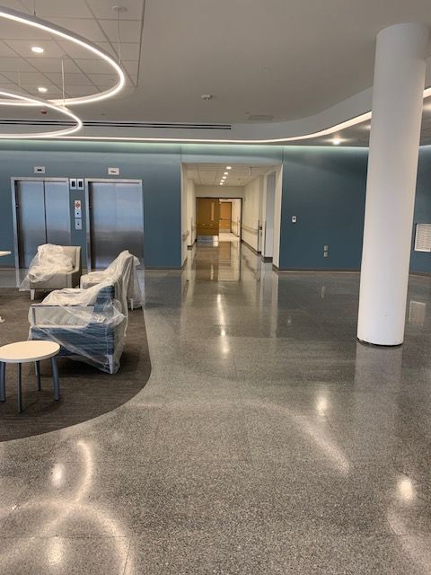 Empty hospital lobby with polished concrete floor, two elevators, blue accent wall, and waiting area.