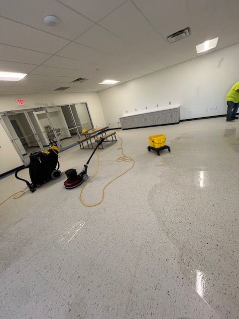 Floor cleaning in progress in a large room with a polished speckled floor.