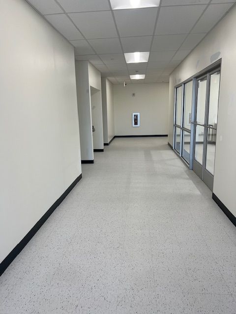 Long hallway with light-colored walls and floor, recessed ceiling lights, and glass doors.