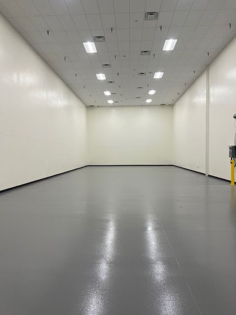 Empty, rectangular room with gray floor, white walls, and ceiling lights.