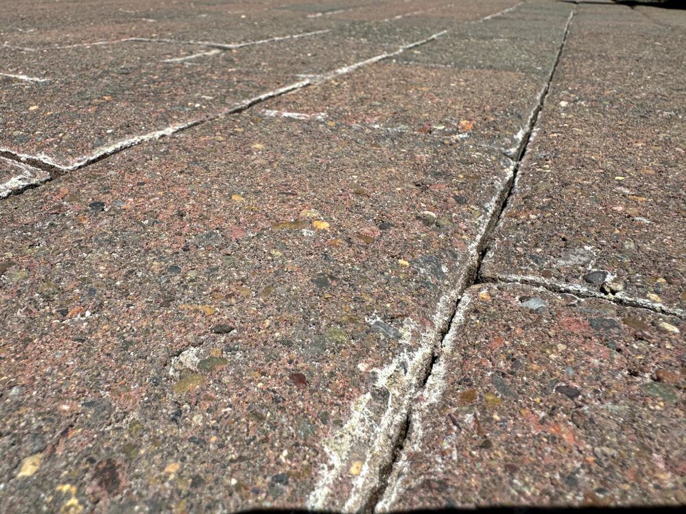 Close-up of a rough stone pavement with cracks and speckled reddish-brown tiles