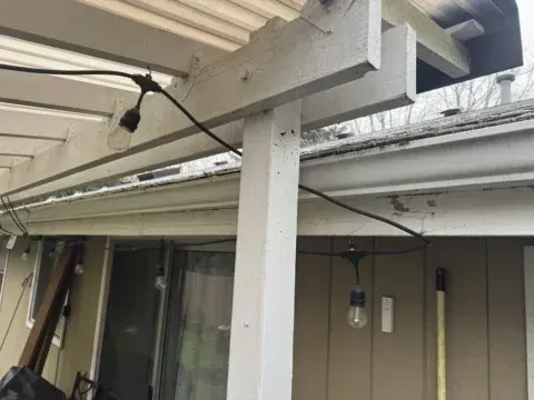 Covered patio with white beams, a support post, hanging light, and sliding glass doors.