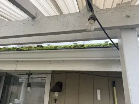 Covered porch roof with white beams, hanging bulb, and house windows below