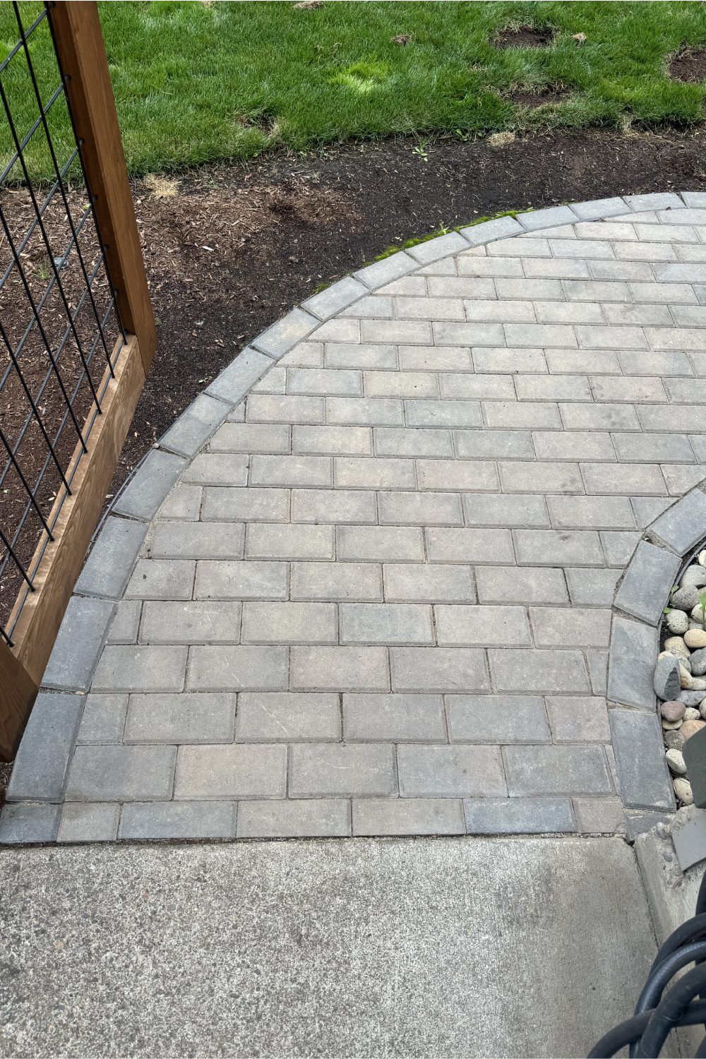 Curved gray brick walkway beside a gravel border, grass, and a wooden fence corner