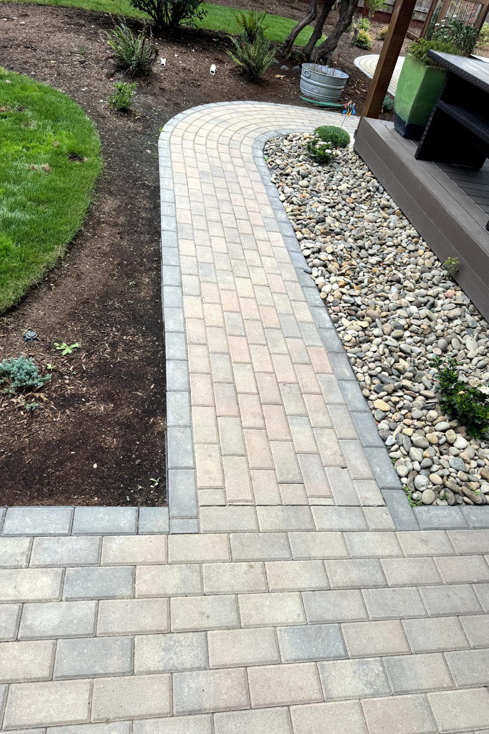 Curved brick garden path beside mulched beds and a gravel strip